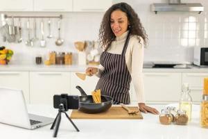mulher latina gravando vídeo e cozinhando na cozinha foto