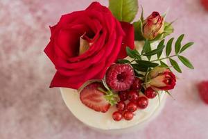 um pequeno bolo de branco e rosa decorado com flores e frutos silvestres foto