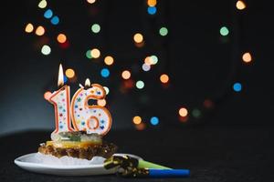 torta de vela acesa de aniversário número 16 com soprador de chifre de festa em um cenário de bokeh iluminado foto
