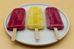 picolés amarelos e roxos em palitos de sorvete em um prato branco foto