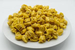 tortellini cru italiano tradicional em um prato, isolado no fundo branco foto