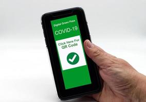 mão segurando um smartphone com um passe digital verde em exibição, pronto para receber o código qr confirmando a vacinação covid-19 foto