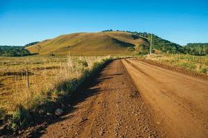 estrada de terra deserta que passa por planícies rurais chamadas pampas com colinas verdes e árvores próximas a cambara do sul. uma pequena cidade do sul do brasil com incríveis atrativos turísticos naturais. foto