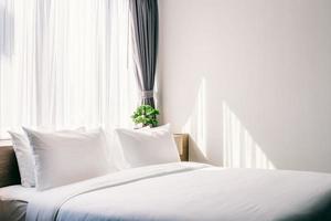 close-up de travesseiro branco na decoração da cama com lâmpada e árvore verde em vasos de flores no interior do quarto do hotel. foto