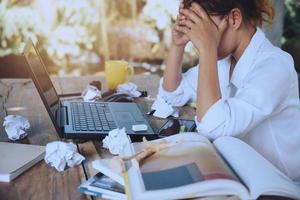 mulher asiática sentada trabalhando em casa nas férias. usar trabalhando com notebook. sentindo muito estressado e dores de cabeça com o trabalho realizado.