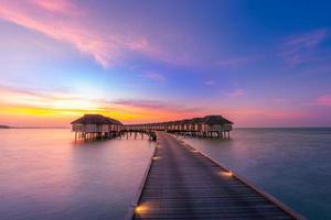 panorama incrível do pôr do sol nas maldivas. luxo resort vilas vista do mar com luzes LED suaves sob o céu colorido. lindo céu crepuscular e nuvens coloridas. fundo de praia lindo para férias de férias
