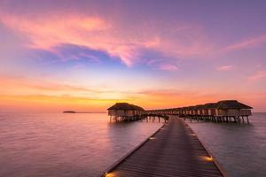 panorama incrível do pôr do sol nas maldivas. luxo resort vilas vista do mar com luzes LED suaves sob o céu colorido. lindo céu crepuscular e nuvens coloridas. fundo de praia lindo para férias de férias foto