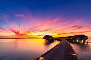 pôr do sol na ilha das Maldivas, resort de villas luxuosas na água e cais de madeira. lindo céu, nuvens e fundo de praia para férias de verão, férias e conceito de viagens foto