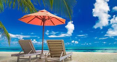 belas paisagens de uma ilha tropical, duas espreguiçadeiras, espreguiçadeiras, guarda-chuva sob uma palmeira. areia branca, vista mar com horizonte, céu azul idílico, sossego e relaxamento. hotel resort de praia inspirador