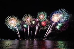 incríveis e lindos fogos de artifício coloridos na noite de celebração, mostrando na praia do mar com reflexo de várias cores na água foto