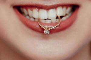 close-up jovem noiva mostrando seu anel de casamento, segurando nos dentes e sorrindo. mulher com anel de diamante e lábios vermelhos.