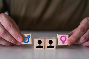 uma escolha entre um homem e uma mulher. as mãos apontam para dois cubos de madeira com um ícone de gênero, um masculino e um feminino.