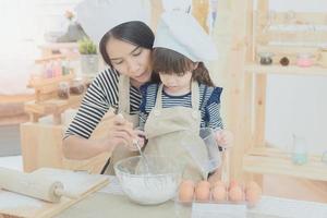 família feliz na cozinha. mãe asiática e a filha dela preparando a massa para fazer um design cake.photo para família, crianças e conceito de pessoas felizes. foto