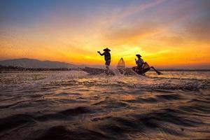 silhueta pescador asiático no barco de madeira, lançando uma rede para a captura de peixes de água doce no rio da natureza no início da manhã, antes do amanhecer. foto