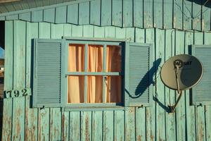 cambara do sul, brasil - 16 de julho de 2019. antena parabólica moderna e janela aberta em casa de madeira velha e gasta ao pôr do sol em cambara do sul. uma pequena cidade do interior com incríveis atrações turísticas naturais. foto