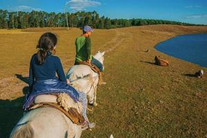 cambara do sul, brasil - 18 de julho de 2019. menina e homem cavalgando em uma paisagem de planícies rurais chamadas pampas ao pôr do sol perto de cambara do sul. uma cidade rural com incríveis atrações turísticas naturais. foto