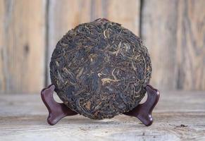 chá tradicional chinês pu-erh em um suporte de madeira. chá fermentado cru na forma de uma panqueca foto