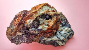 andesito ígneo alterado em zona de alteração hidrotermal, com veios de quartzo, clorita e minerais de pirita preta brilhante, sobre fundo rosa. Indonésia, exploração geológica.