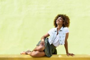 jovem negra, penteado afro, sentada em uma parede urbana foto