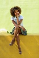 jovem negra, penteado afro, sentada em uma parede urbana foto