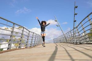 mulher com penteado afro de patins, andando ao ar livre na ponte urbana foto