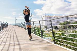 mulher com penteado afro de patins, andando ao ar livre na ponte urbana foto