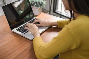 conceitos de tecnologia de negócios - estilo de vida digital trabalhando fora do escritório. mulher com as mãos digitando o computador portátil com uma tela em branco na mesa na cafeteria. simulação de tela de laptop em branco para exibição de design foto