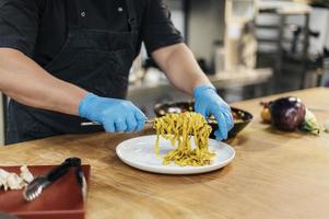 chef masculino com luvas colocando prato de macarrão foto