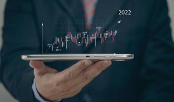empresário segurando a previsão de previsão do mercado de ações do tablet 2022, gráficos e castiçais, tendência de movimento do mercado de ações, do passado ao presente. foto