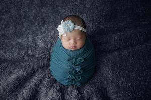 pequeno bebê recém-nascido envolto em um lenço azul com uma bandagem na cabeça deitado sobre um cobertor macio foto