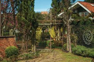 gramado, brasil - 21 de julho de 2019. entrada com jardim exuberante e portão de ferro fechado de uma casa em um dia de sol no gramado. uma linda cidade de influência europeia, muito procurada por turistas. foto