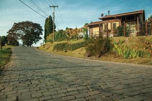 bento goncalves, brasil - 13 de julho de 2019. estrada de pedra em frente a uma charmosa casa de madeira com jardim ao pôr do sol perto de bento goncalves. foto