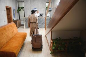 elegante o negócio mulher com viagem carrinho bagagem dentro hotel lobby foto