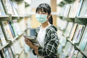 uma mulher usando uma máscara e procurando livros na biblioteca. foto
