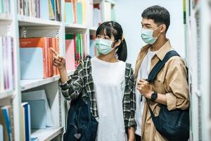 homens e mulheres carregando mochilas e procurando livros na biblioteca. foto