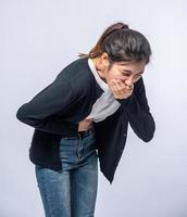 uma mulher com dor de estômago coloca as mãos na barriga e cobre a boca.