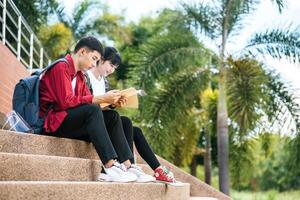 estudantes do sexo masculino e feminino sentados e lendo livros nas escadas. foto