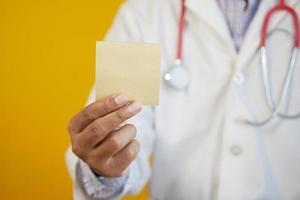 a mão do médico segura um post-it contra um fundo amarelo foto