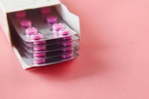 close up de pílulas de blister em um pacote de papel no fundo rosa foto