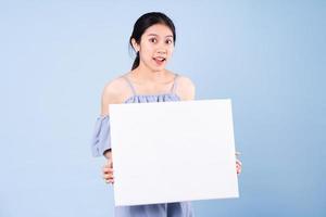 imagem de menina asiática segurando um quadro branco, isolado em um fundo azul foto