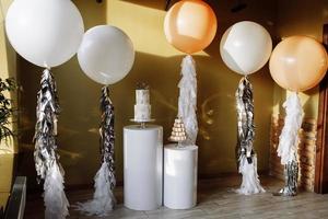 primeiro aniversário elegante bolo branco. bolo de três histórias infantil na primeira festa de aniversário no fundo das bolas. Barra de chocolate. o primeiro bolo. foco seletivo foto