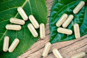 cápsulas de ervas naturais de medicamentos fitoterápicos em folha verde e fundo rústico foto