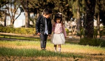 menino e menina brincando e andando no parque perto da floresta de mãos dadas foto