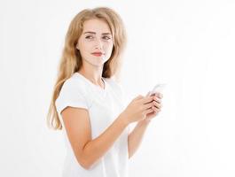 jovem mulher bonita em t-shirt usando seu smartphone isolado no fundo branco. garota loira sexy conversando com um amigo ou fazendo compras online. copie o espaço