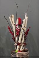 vela vermelha de natal decorada com um monte de galhos de madeira e frutas e cones de abeto em um fundo cinza