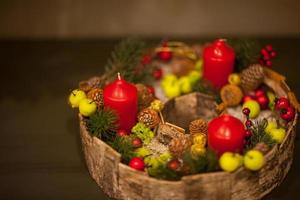 vela vermelha de Natal em uma cesta com frutas e cones de abeto com maçãs verdes foto