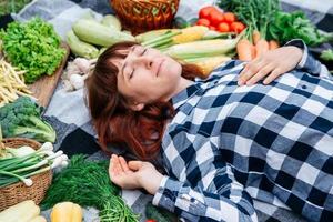 mulher com os olhos fechados deitada sobre uma manta entre vegetais orgânicos frescos foto