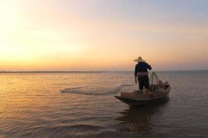 pescador asiático com seu barco de madeira indo para pegar peixes de água doce no rio da natureza no início durante o nascer do sol