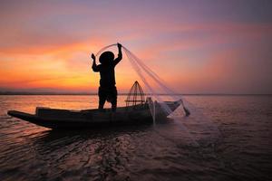 pescador asiático com seu barco de madeira no rio da natureza no início da manhã antes do nascer do sol foto