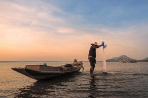pescador asiático com barco de madeira no rio da natureza no início da manhã antes do nascer do sol foto